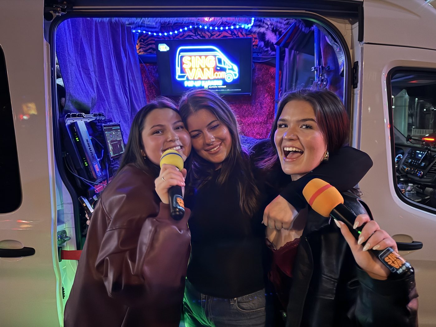 Three friends enjoying karaoke with microphones at the neon-lit SingVan